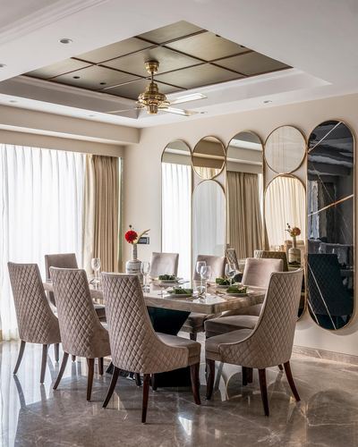 Art deco dining room with brass coffered ceiling and mixed-shape mirror wall behind quilted chairs