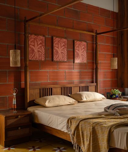 Four-poster wood bed against terracotta brick wall with cane pendant lights and framed botanical panels