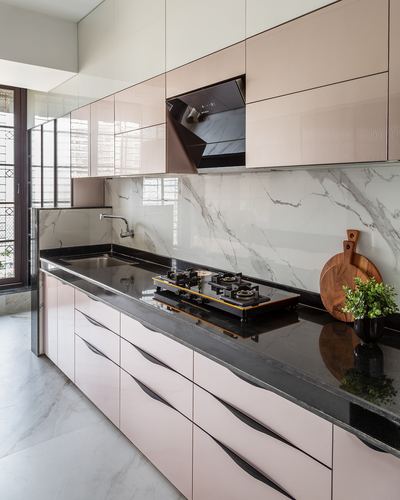Galley kitchen with blush pink glossy cabinets, black granite counter, marble-look backsplash, and a gas hob.