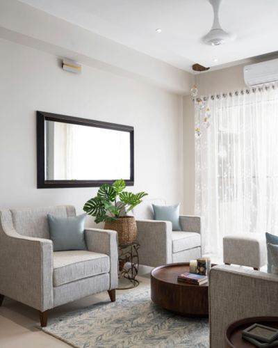 Neutral living room with grey armchairs, round wood coffee table, mirror and sheer curtains