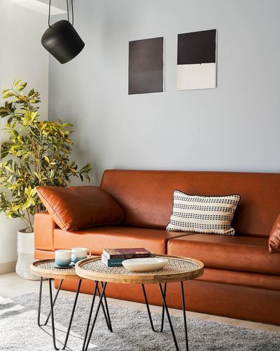 Rust leather sofa against grey wall with black and white art, cane-topped nesting tables in front