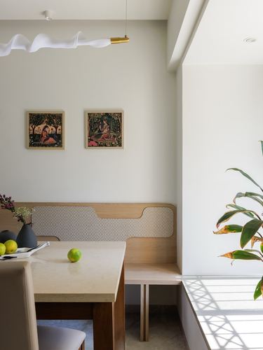 Wood-framed dining banquette with patterned cushions beneath framed miniature paintings, stone table in foreground