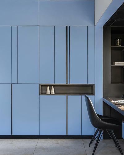 Blue paneled cabinetry wall with recessed niche beside a black leather chair and desk