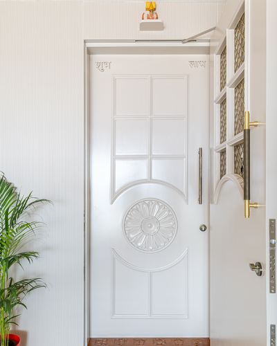 White carved wooden entrance door with floral medallion and brass handle, foyer with plant