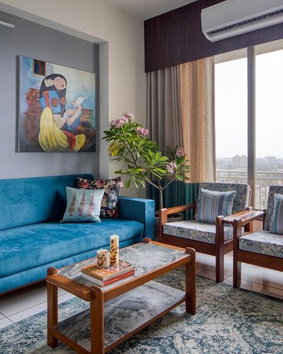 Living room with teal velvet sofa, wooden coffee table, cane armchairs and a figurative painting on grey niche.