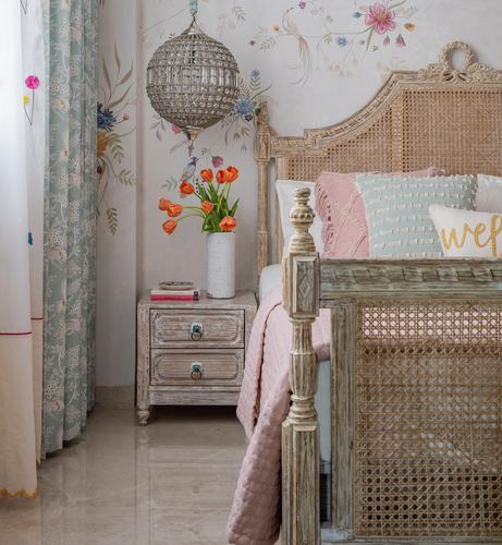 Carved cane bed with pink cushions beside floral mural wall and beaded globe pendant light