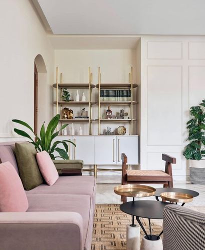 Pink velvet sofa with olive and blush cushions facing a brass-framed open shelving unit in a cream living room