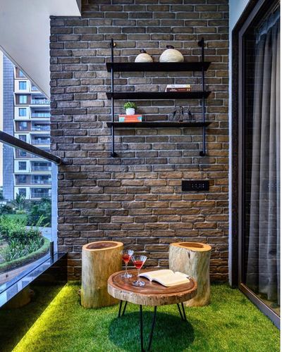 Balcony with exposed brick wall, pipe shelving, tree-stump stools and live-edge table on faux grass
