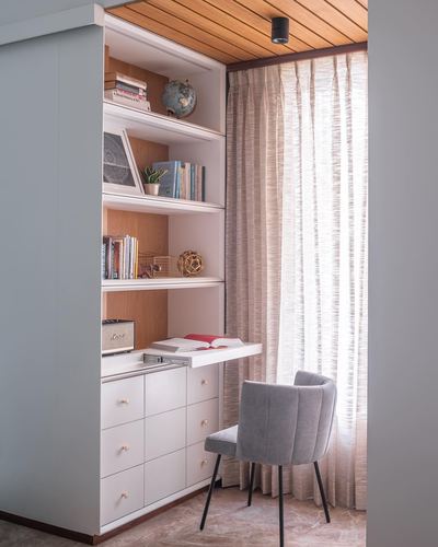 Built-in white shelving unit with desk and grey chair beside sheer curtained window