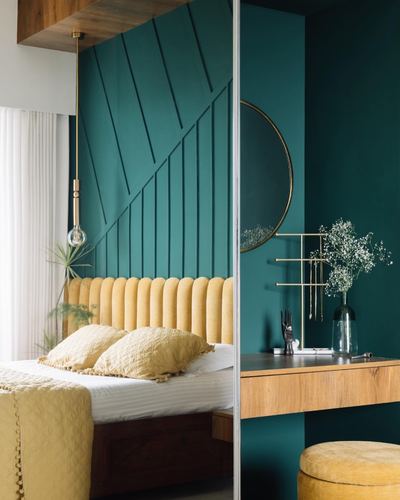 Teal bedroom with mustard channel-tufted headboard beside a teal dressing nook with round mirror