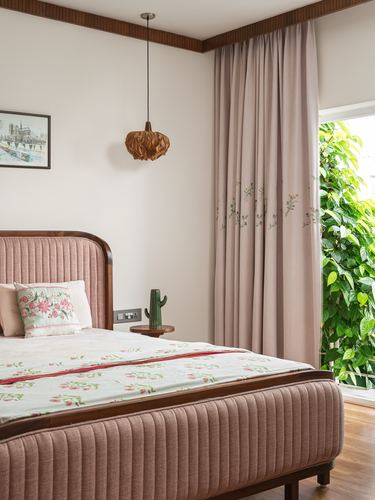 Pink upholstered bed with wood trim, woven pendant light, and curtained doorway to greenery