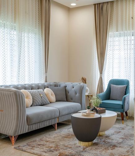 Beige living room with grey tufted sofa, teal armchair, and round nesting coffee tables on a patterned rug