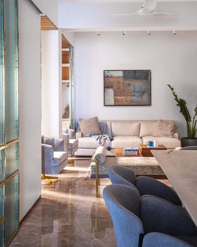 Living room with cream sofa, blue chairs, marble floor and a fluted glass brass partition
