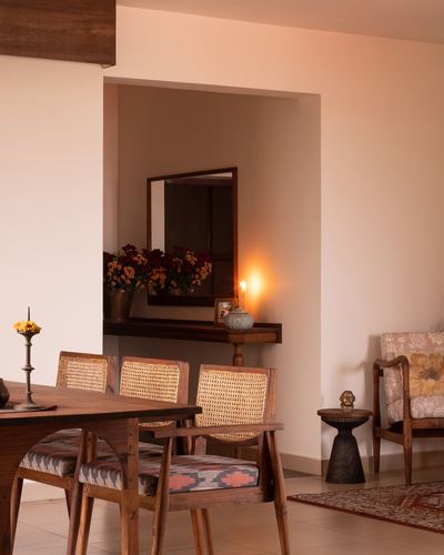 Dining table with cane chairs in foreground, glowing alcove with mirror and flowers beyond