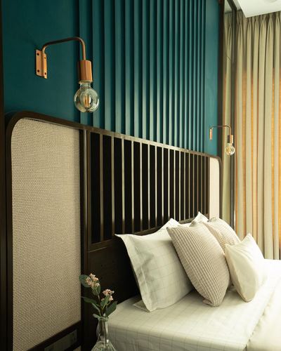 Bed with dark wood and cane headboard against a teal vertical-slat wall with brass sconces