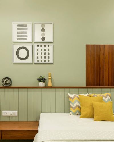 Sage green bedroom with fluted wood headboard, mustard cushions, and framed abstract art above a wooden ledge