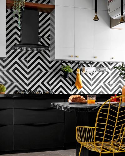 Black and white chevron-tiled kitchen with black cabinetry and a yellow wire chair at a marble breakfast counter