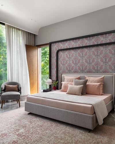 Bedroom with pink patterned wallpaper headboard wall, grey upholstered bed, and floor-to-ceiling garden view