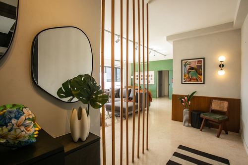 Foyer with wood slat screen, organic mirror, monstera plant, and glimpse into green-walled living room