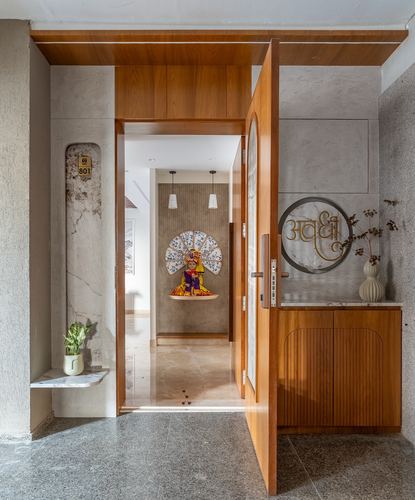 Entry foyer with wooden pivot door open to a corridor with pendant lights and deity artwork