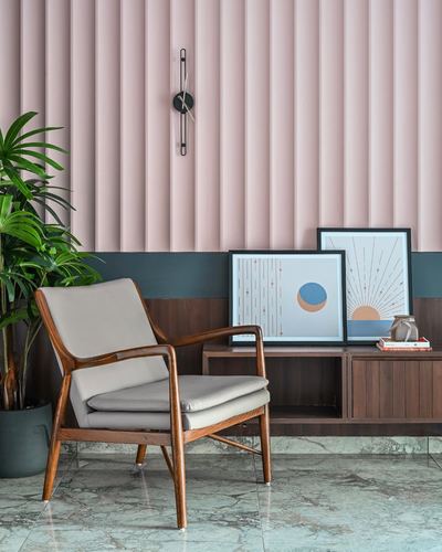 Mid-century wooden armchair beside a low console with framed art against a pink fluted wall