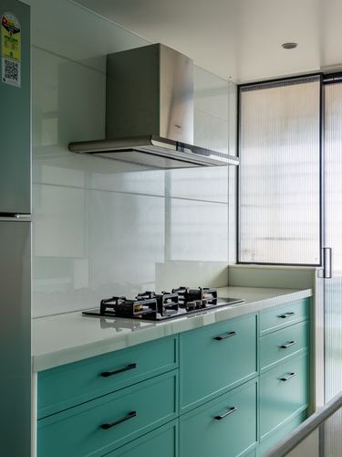 Modern kitchen counter with teal cabinets, stainless hood, and fluted glass window