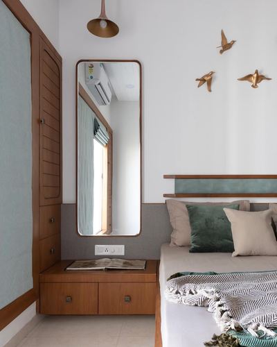 Bedroom corner with wooden wardrobe, tall mirror, brass bird wall decor and green-toned bed linen