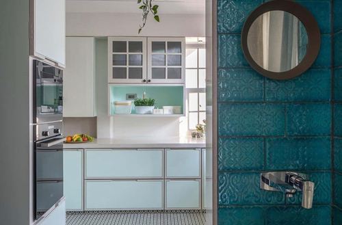 Mint pastel kitchen with glass cabinets beside a teal textured tile wall and round mirror