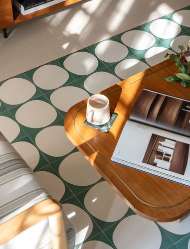 Overhead view of a rounded wooden side table with mug and magazine on green patterned tile floor