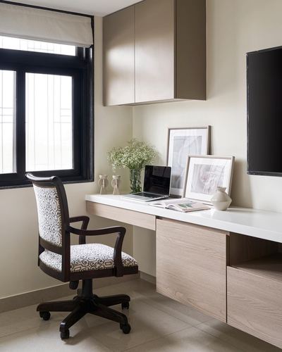 Wall-mounted study desk with laptop, framed prints, and a patterned upholstered office chair below a tv