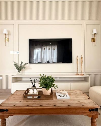 Cream fluted panel wall with mounted tv, brass sconces, and a rustic wood coffee table in living room