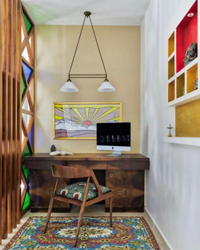 Small study nook with wooden desk, iMac, sunrise artwork, and colorful stained-glass partition in Mumbai home