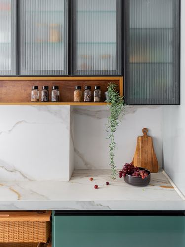 Marble kitchen counter with spice jars, trailing plant and grapes below reeded glass cabinets