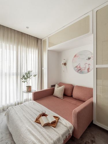 Pink daybed with cushions beneath cane-paneled cabinetry, sheer curtains and round wall art beside.