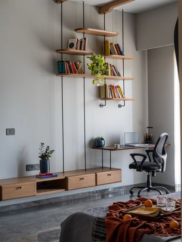 Suspended wooden shelves with books above a floating desk and chair, grey stone floor.