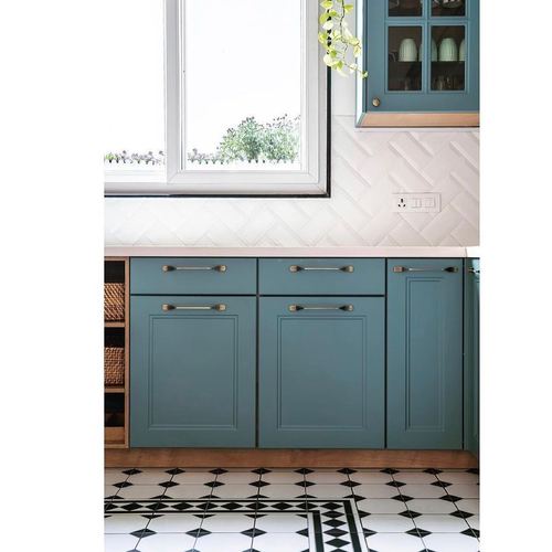 Teal kitchen cabinetry under a window with herringbone tile backsplash and black-and-white patterned floor