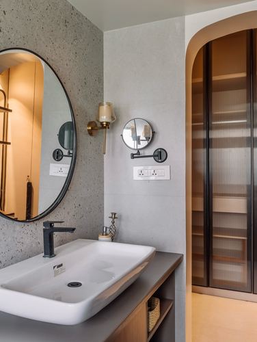 Bathroom vanity with round black-framed mirror, brass sconce, white vessel sink, and arched fluted-glass wardrobe niche.