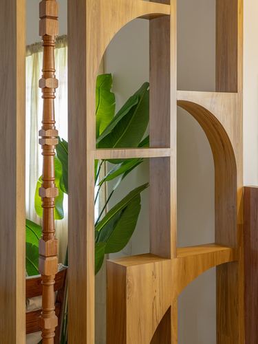 Carved wooden arched partition with plant leaves visible through openings, turned pillar behind