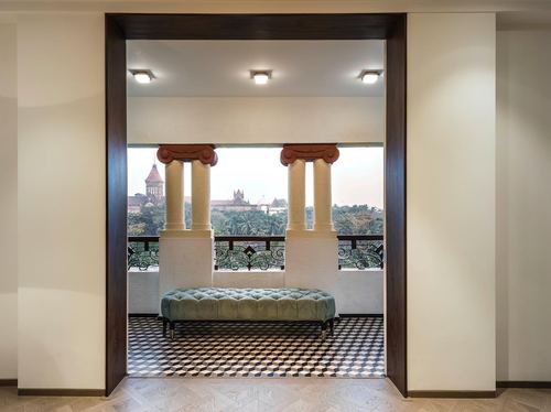 View through dark wood doorway to a balcony with classical columns, tufted green bench, and patterned tile floor.