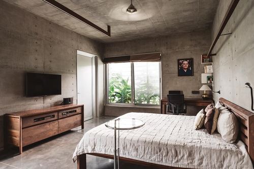 Concrete bedroom with wood-framed bed, tv console, and window seat with greenery view