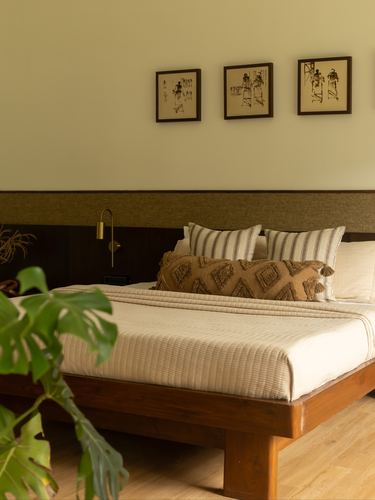 Wooden platform bed with striped linens and diamond-pattern bolster under three framed prints