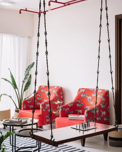 Two red zebra-print swing chairs hang from chains beside a wooden coffee table with a chess set