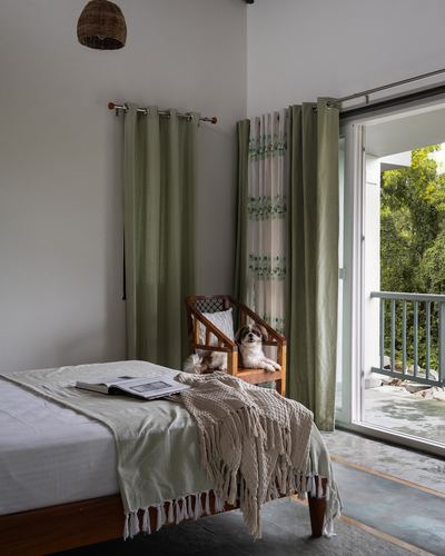 Bedroom with sage curtains, wooden bed, dog on cane chair by open balcony door