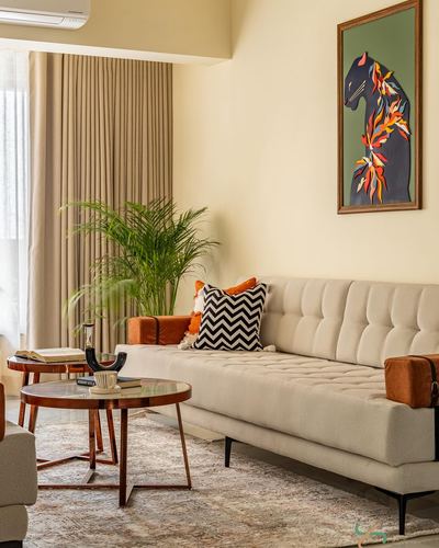 Beige tufted sofa with orange cushions beside round wood coffee tables and a framed panther artwork