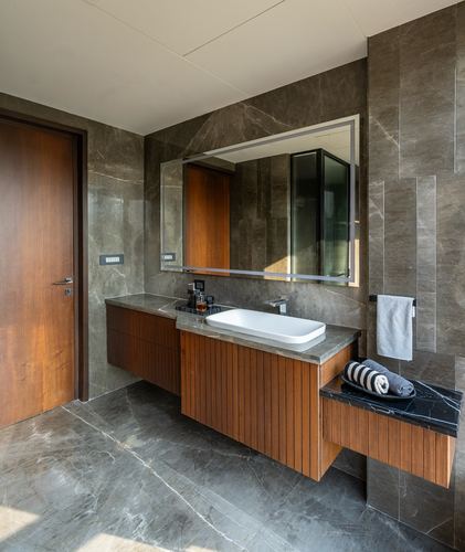 Bathroom vanity with ribbed wood cabinetry, stone countertop, vessel sink and backlit mirror against dark stone walls