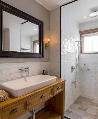 White subway-tiled bathroom with wooden vanity dresser and glass-enclosed shower