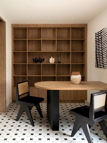 Wooden open shelving unit behind an oval dining table with black cane chairs on patterned tile floor