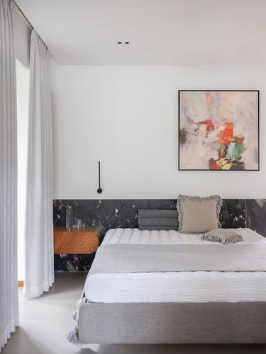 Minimalist bedroom with grey upholstered bed, dark stone accent wall, and abstract painting