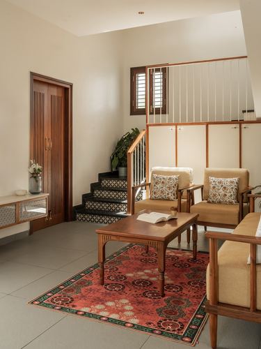 Living room with staircase, wooden armchairs, coffee table and patterned rug under natural light