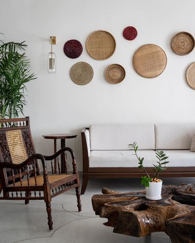Living room with woven basket wall art, cane armchair, sofa, and root coffee table